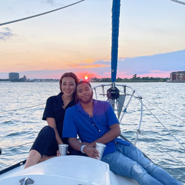 young couple smiling and taking a photo on a boat during a sunset
