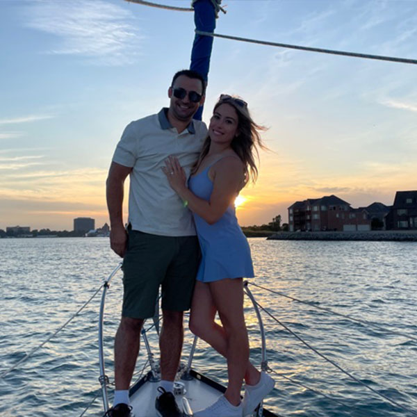 young couple smiling and standing at the head of the boat during a sunset